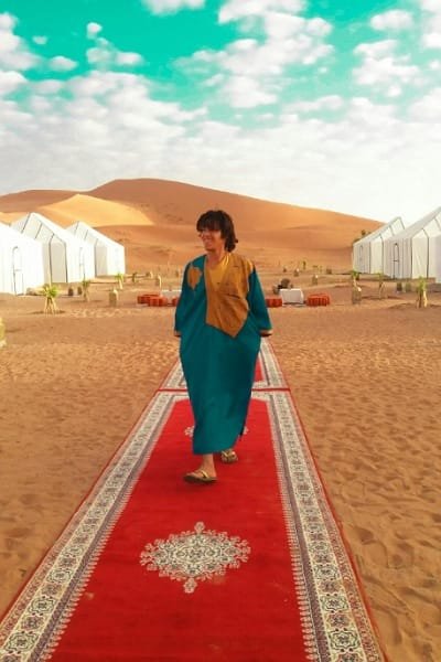 Tourist walking on a luxurious red carpet near a glamping tent, reflecting a premium, comfortable stay experience in the Merzouga Sahara Desert.