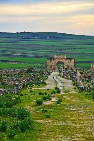 A massive stone wall structure with archways, likely from the historical ruins of Volubilis or a monumental gate in Meknes, illustrating the grand architecture on the Fes day trip.