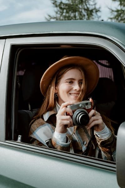 A happy female tourist wearing a hat smiles while taking a photo from the comfort of a private and group, air-conditioned tour vehicle, emphasizing the smooth, luxury travel experience in Fes.