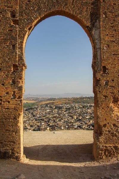 A vertical photo of the massive facade of Borj Nord (North Tower) in Fes, showcasing the imposing Islamic defensive architecture and stone walls, with visitors passing through the archway.