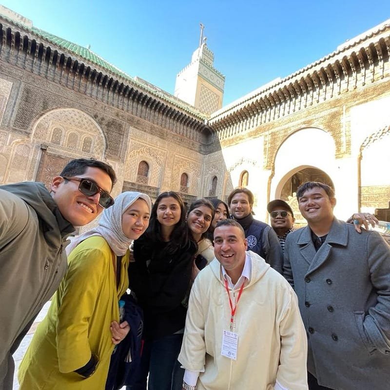 A collage of smiling tourists and local guides taking selfies and group photos across Fes, including the medina's souks and historical courtyards, showcasing the fun group tour experience.