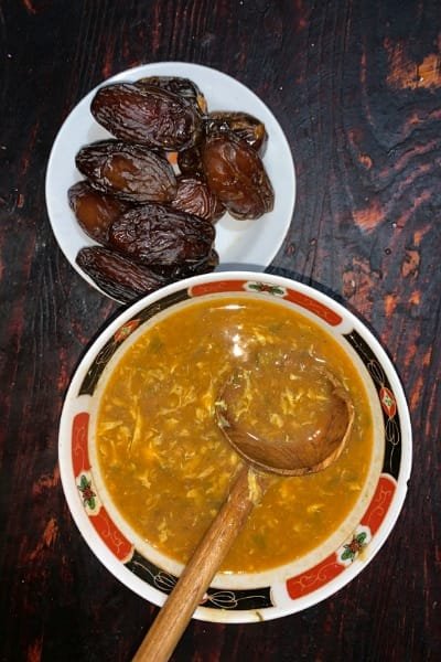 A bowl of authentic Moroccan Harira soup served with a spoon and a plate of fresh dates on a dark wooden table, highlighting a warm, traditional meal stop on the Fes Food Tour.