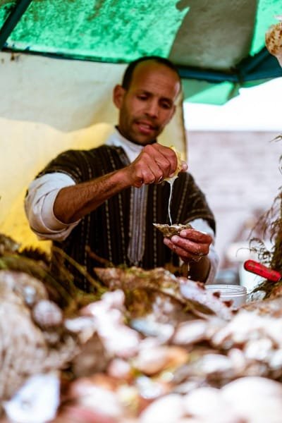 A local Fes street vendor in traditional attire squeezing fresh lemon juice onto an oyster, showcasing the diverse and fresh seafood offerings during a Fes food tasting tour.